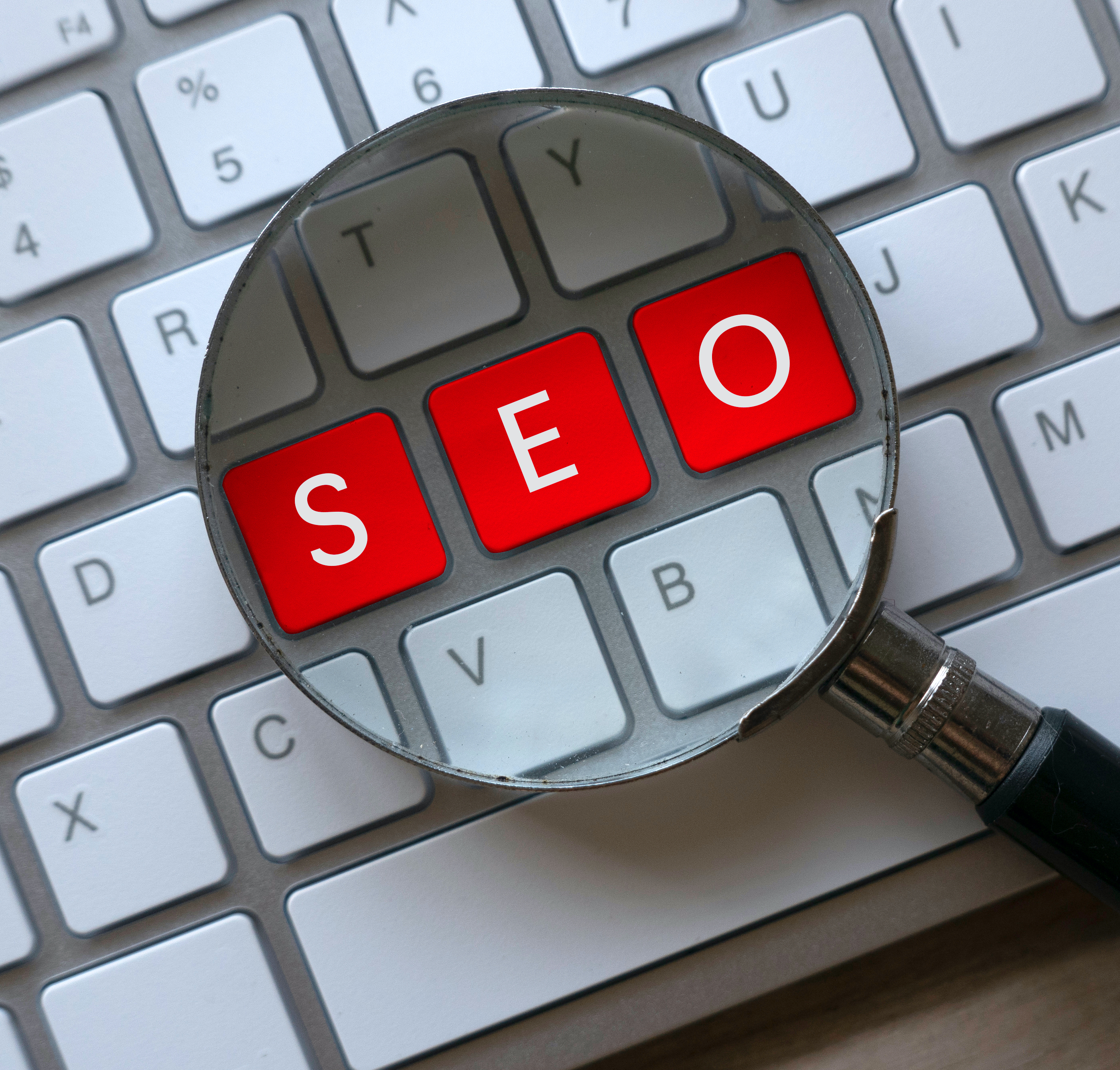 SEO written on a keyboard with a magnifying glass on top to symbolize search