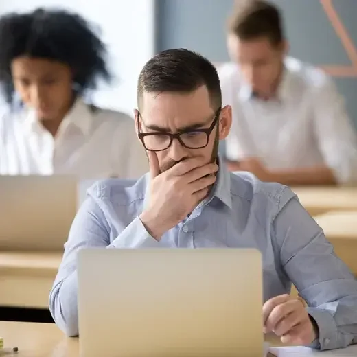 Marketer frowning at a laptop while colleagues work behind him