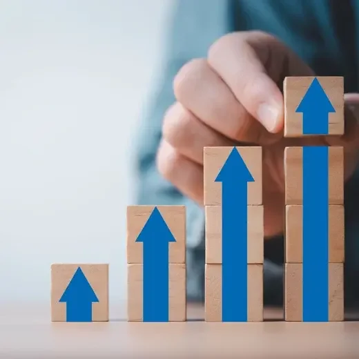 Hand placing wooden blocks with rising blue arrows to show business growth