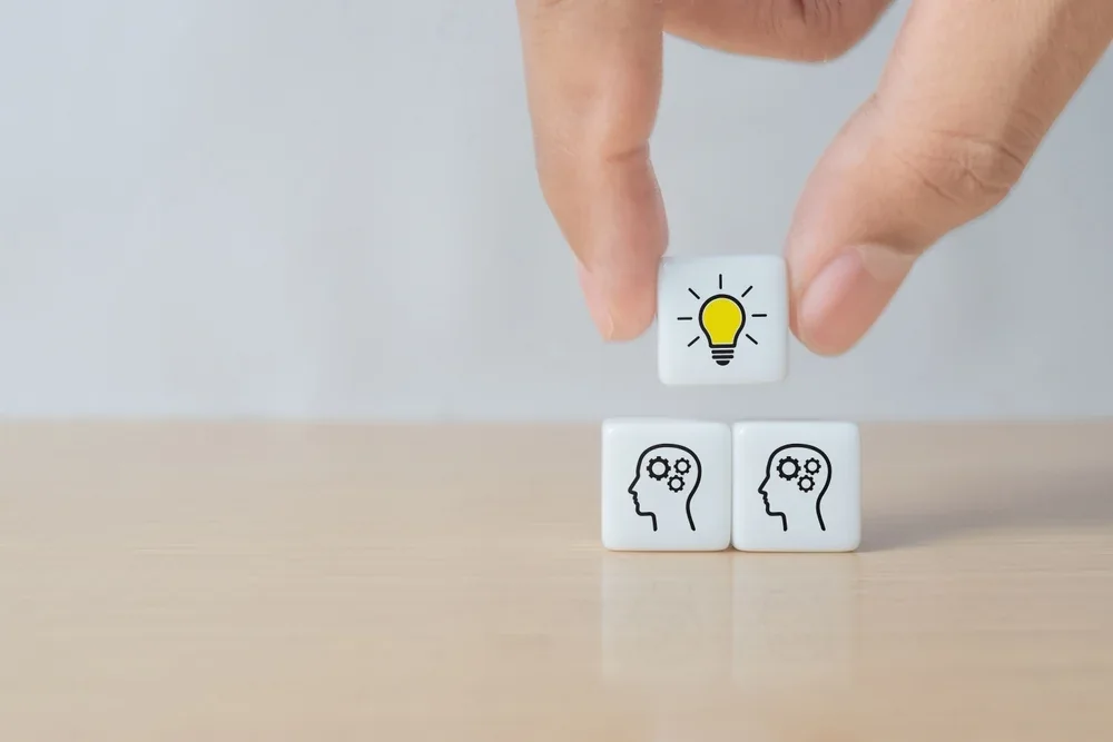 Hand placing a lightbulb block above two blocks showing heads with gears
