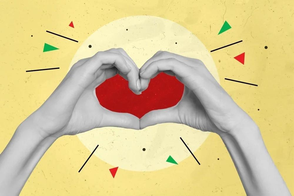 Hands forming a heart shape around a red paper heart