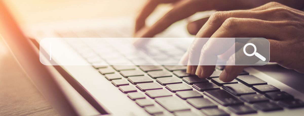 Hands typing on a laptop keyboard with search bar overlay