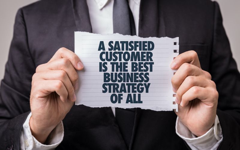 Business owner holding a sign that says a satisfied customer is the best business strategy