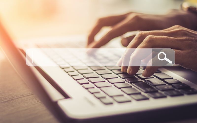 Hands typing on a laptop keyboard with search bar overlay