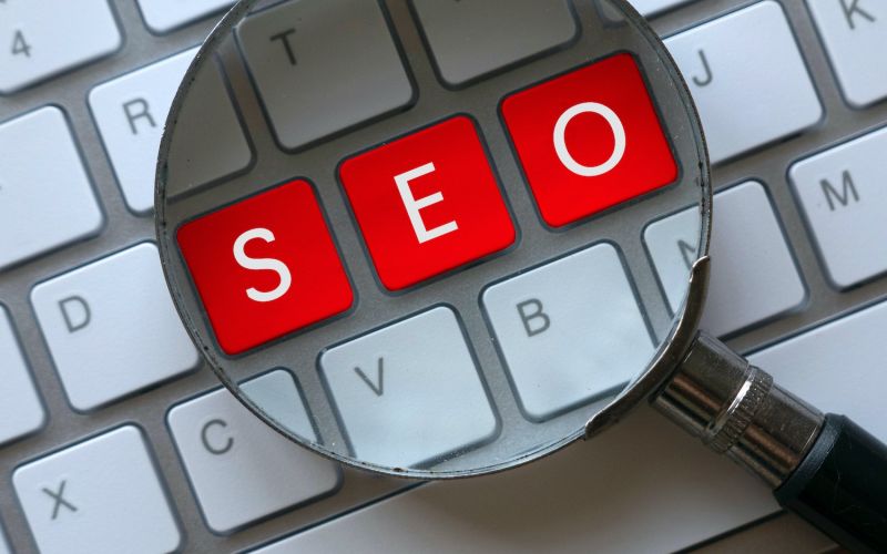 SEO written on a keyboard with a magnifying glass on top to symbolize search